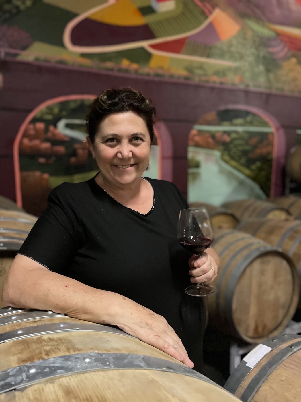 Fiorella Bertino in cantina, tra le botti, con un bicchiere di rosso in mano